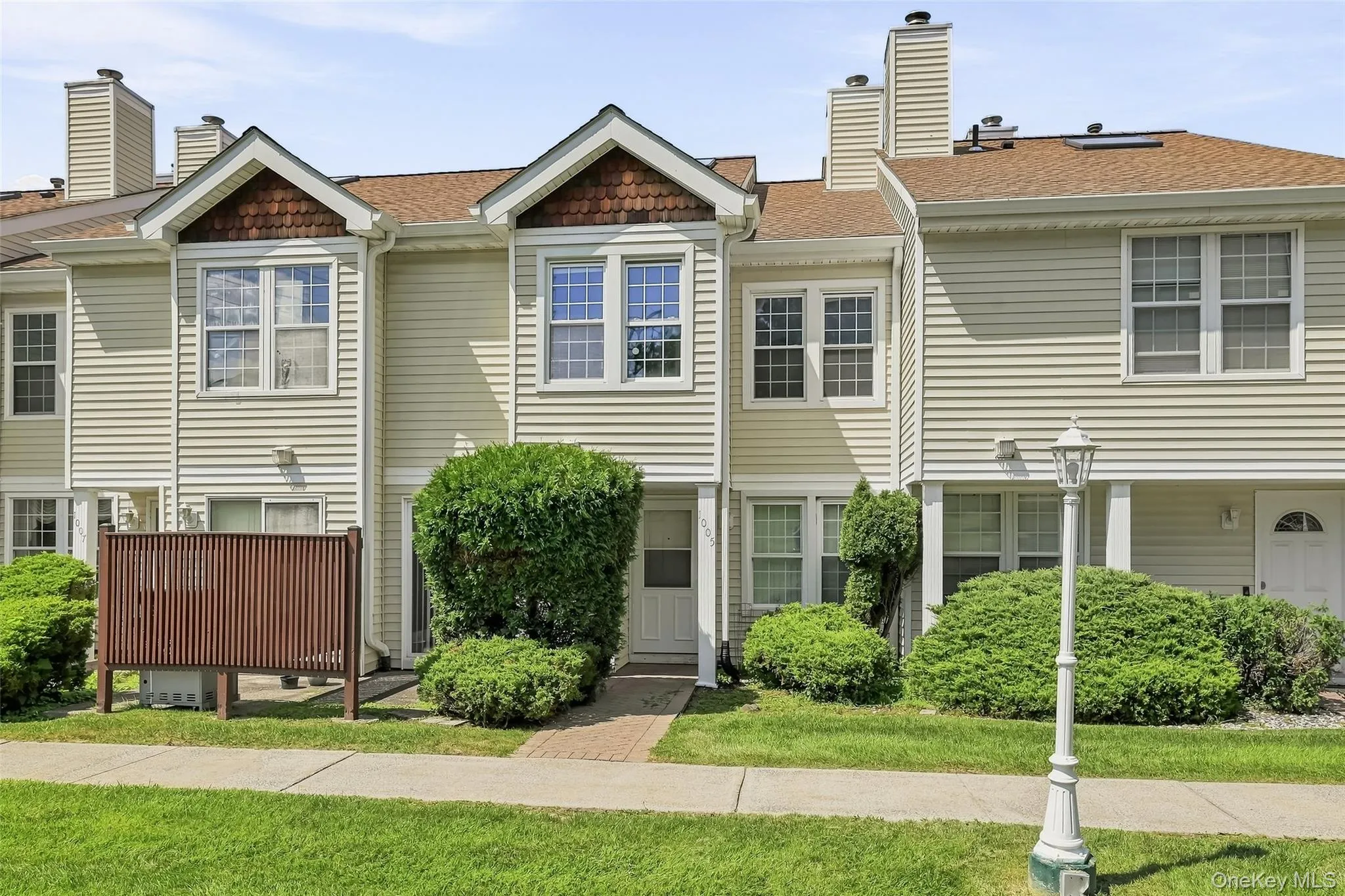 Two-story townhome with light-colored siding, brick walkway, and gabled roofline Two-story townhome with light-colored siding, brick walkway, and gabled roofline