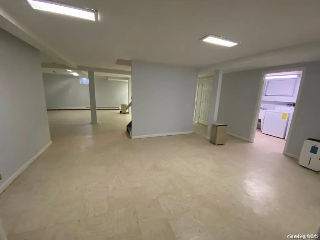 Expansive open-concept room with light-toned flooring, recessed lighting, and a dedicated laundry area featuring a stackable washer and dryer Expansive open-concept room with light-toned flooring, recessed lighting, and a dedicated laundry area featuring a stackable washer and dryer