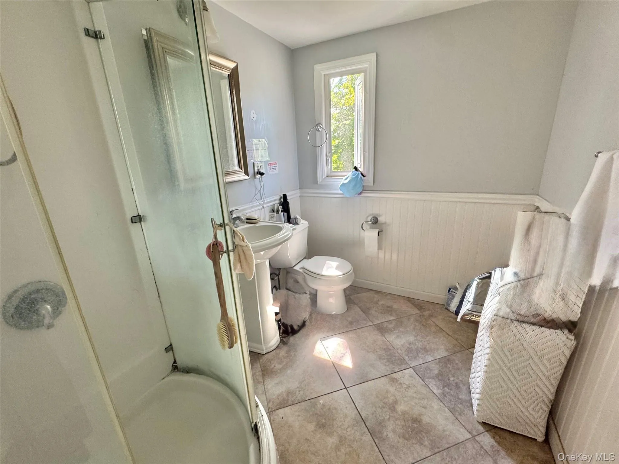 Second Floor Bathroom. Pedestal sink, tile flooring, glass-enclosed shower, white wainscoting, and a window for natural light Second Floor Bathroom. Pedestal sink, tile flooring, glass-enclosed shower, white wainscoting, and a window for natural light