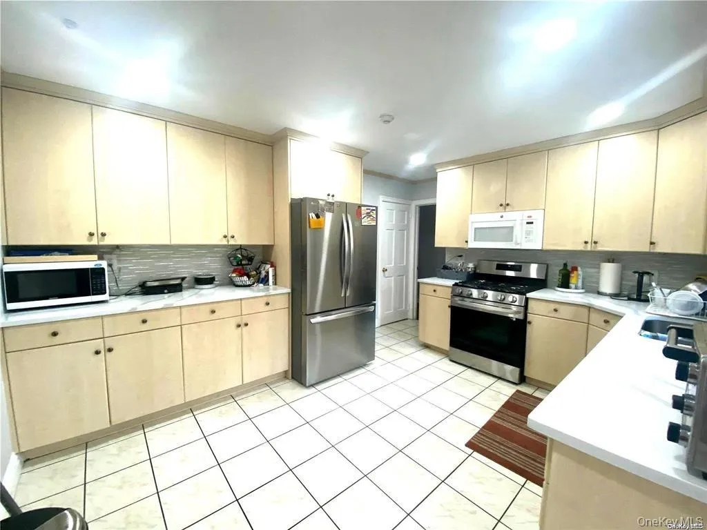 Light-toned cabinetry with matching upper and lower storage, white countertops, tile flooring, and a subway tile backsplash Light-toned cabinetry with matching upper and lower storage, white countertops, tile flooring, and a subway tile backsplash