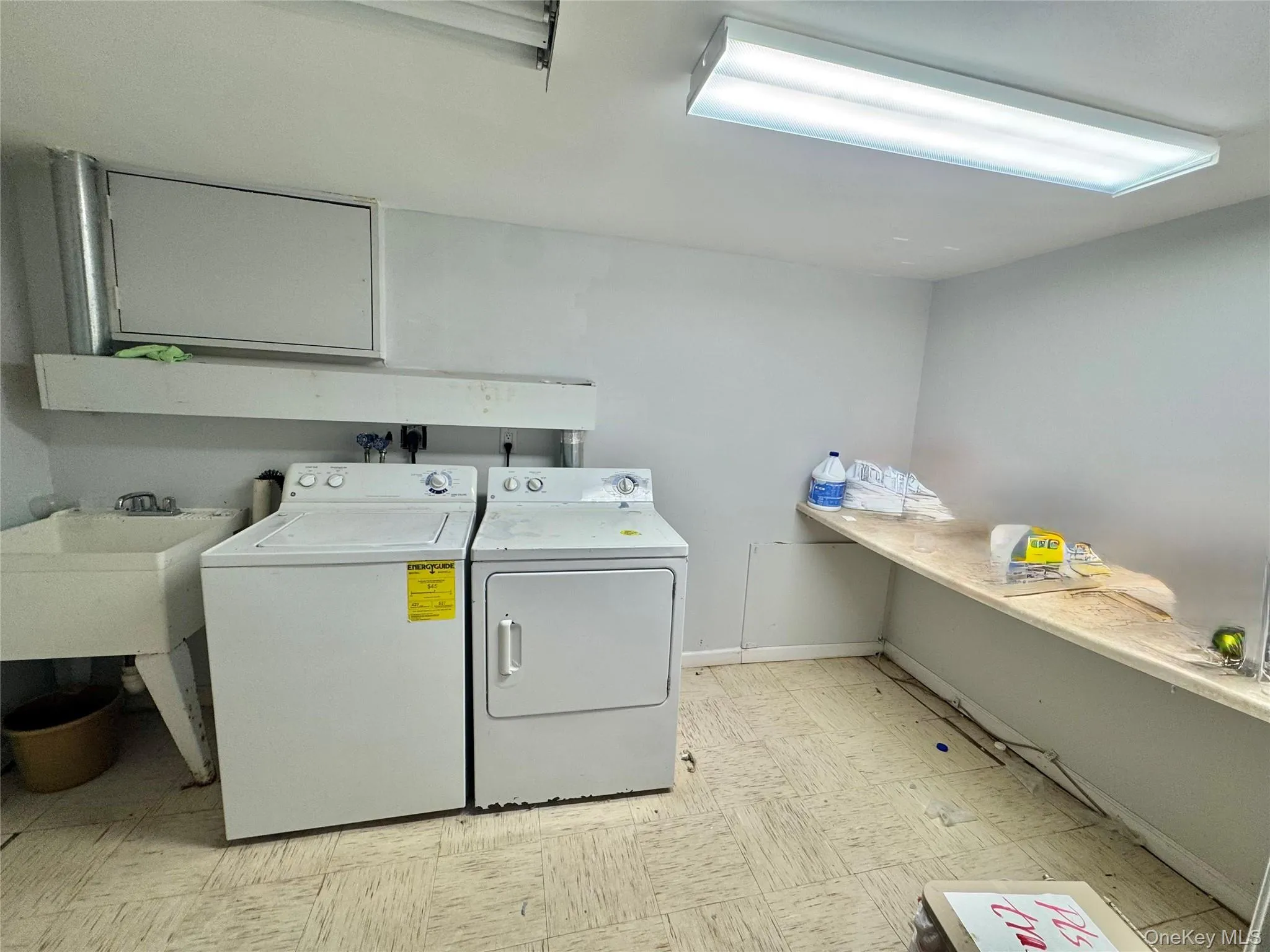 Utility room with a built-in utility sink, overhead fluorescent lighting, and a long built-in shelf Utility room with a built-in utility sink, overhead fluorescent lighting, and a long built-in shelf