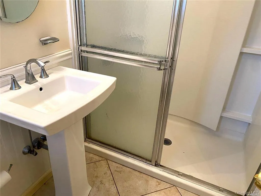 Pedestal sink with brushed metal faucet, framed shower enclosure with frosted glass, and tiled flooring Pedestal sink with brushed metal faucet, framed shower enclosure with frosted glass, and tiled flooring