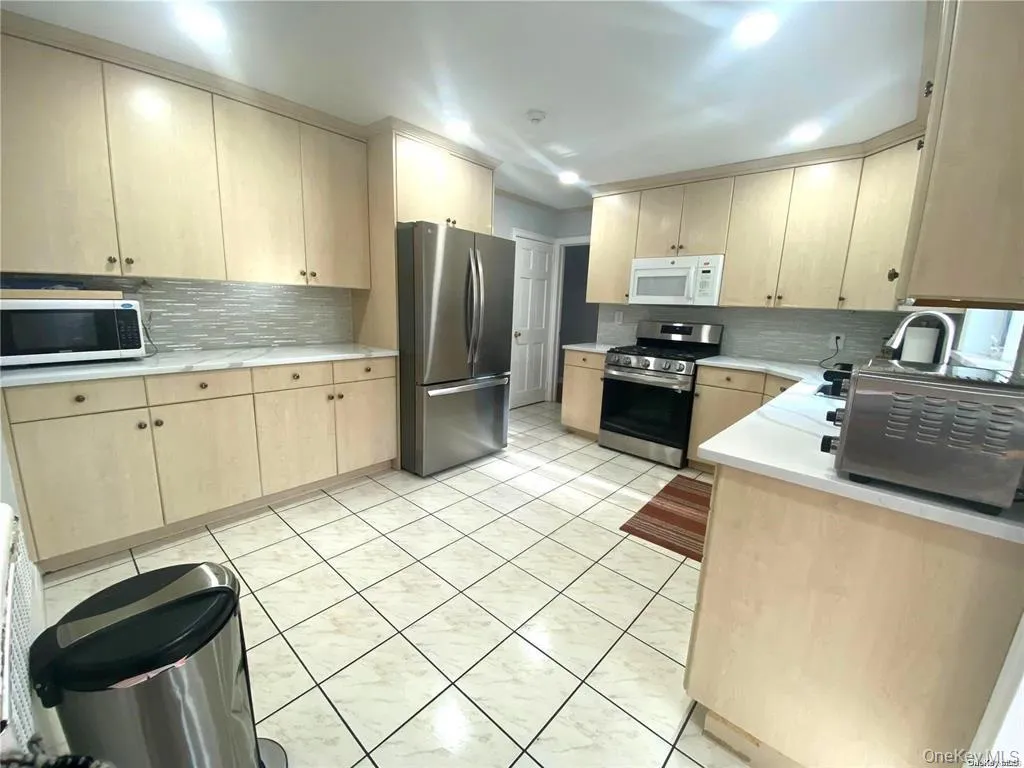 Expansive kitchen featuring light wood-finish cabinetry, stainless steel appliances, a tile backsplash, and light-colored countertops Expansive kitchen featuring light wood-finish cabinetry, stainless steel appliances, a tile backsplash, and light-colored countertops
