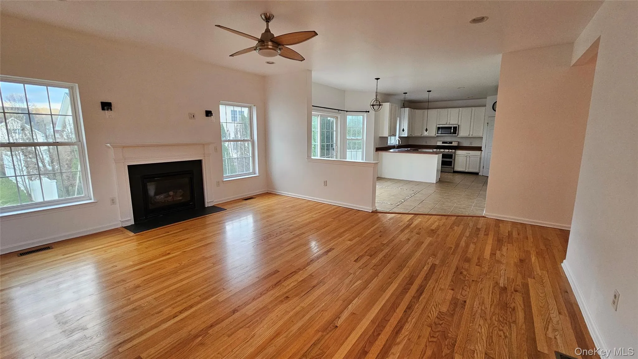 Family room with a fireplace with flush hearth, light wood-style flooring, a ceiling fan, visible vents, and baseboards Family room with a fireplace with flush hearth, light wood-style flooring, a ceiling fan, visible vents, and baseboards
