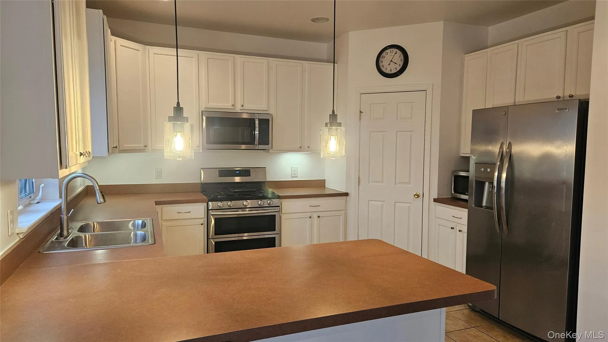 Kitchen with light tile patterned floors, a peninsula, white cabinets, appliances with stainless steel finishes, and a sink Kitchen with light tile patterned floors, a peninsula, white cabinets, appliances with stainless steel finishes, and a sink