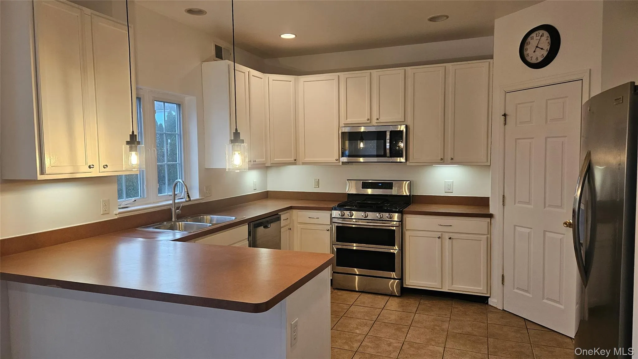 Kitchen featuring light tile patterned floors, a peninsula, white cabinetry, appliances with stainless steel finishes, and a sink Kitchen featuring light tile patterned floors, a peninsula, white cabinetry, appliances with stainless steel finishes, and a sink