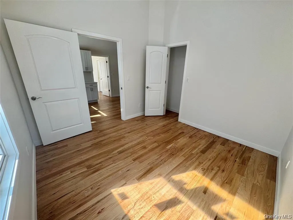 Bright, High Ceiling open room featuring warm wood-finish flooring throughout, multiple white panel doors providing access to adjoining spaces, and abundant natural light from windows along the perimeter Bright, High Ceiling open room featuring warm wood-finish flooring throughout, multiple white panel doors providing access to adjoining spaces, and abundant natural light from windows along the perimeter