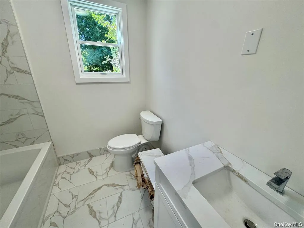 Contemporary bathroom featuring marble-look porcelain tile flooring, a white porcelain toilet with elongated bowl, and a soaking tub with chrome fixtures Contemporary bathroom featuring marble-look porcelain tile flooring, a white porcelain toilet with elongated bowl, and a soaking tub with chrome fixtures