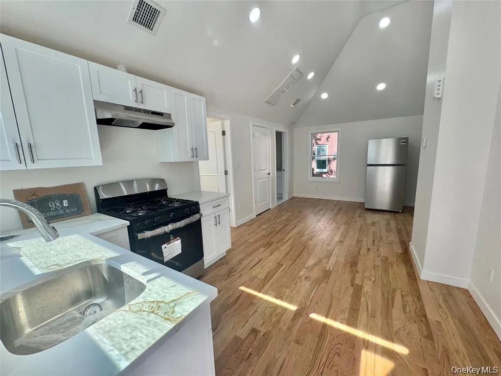 Modern kitchen featuring white cabinetry, stainless steel appliances including a gas range and refrigerator, undermount sink with quartz countertops, recessed lighting, and wood-finish flooring throughout the open-concept living space Modern kitchen featuring white cabinetry, stainless steel appliances including a gas range and refrigerator, undermount sink with quartz countertops, recessed lighting, and wood-finish flooring throughout the open-concept living space