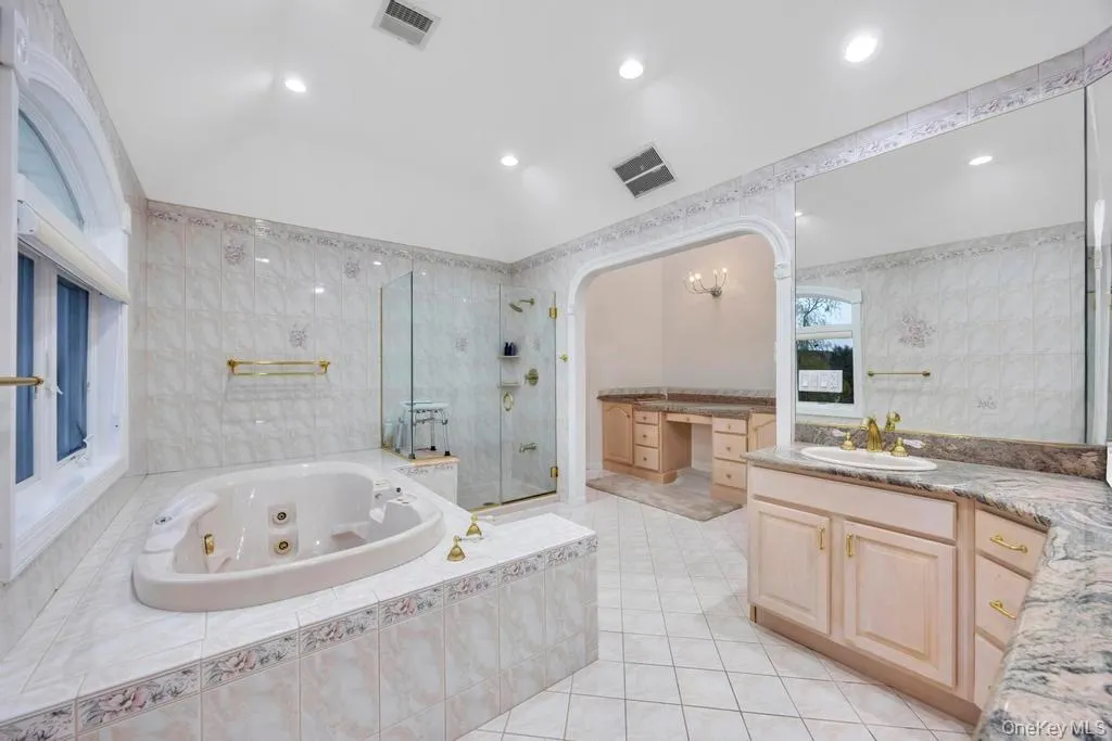 Full bathroom featuring vanity, a jetted tub, a shower stall, tile walls, and light tile patterned floors Full bathroom featuring vanity, a jetted tub, a shower stall, tile walls, and light tile patterned floors