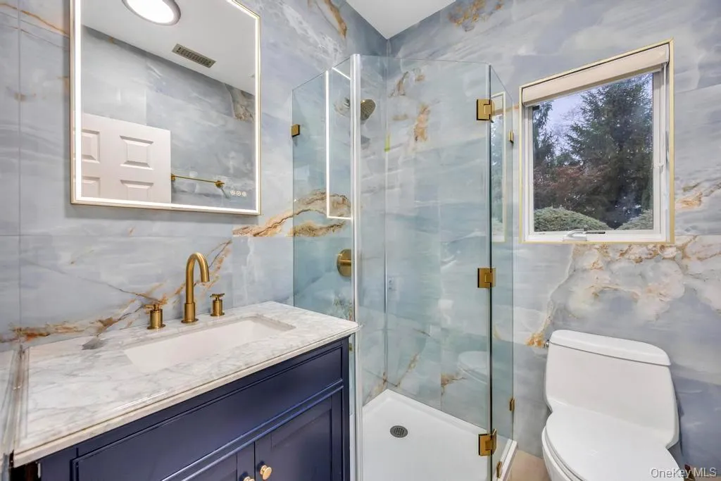 Bathroom featuring tile walls, a marble finish shower, and vanity Bathroom featuring tile walls, a marble finish shower, and vanity
