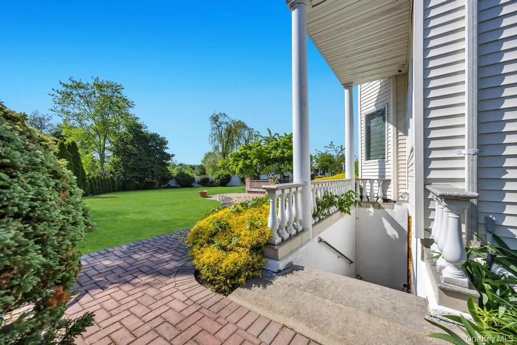 Expansive green lawn surrounded by mature trees, featuring a brick paver pathway leading to a porch with white columns and balusters Expansive green lawn surrounded by mature trees, featuring a brick paver pathway leading to a porch with white columns and balusters