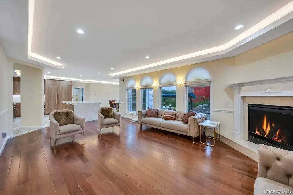 Living room featuring a tray ceiling, recessed lighting, wood finished floors, and a premium fireplace Living room featuring a tray ceiling, recessed lighting, wood finished floors, and a premium fireplace
