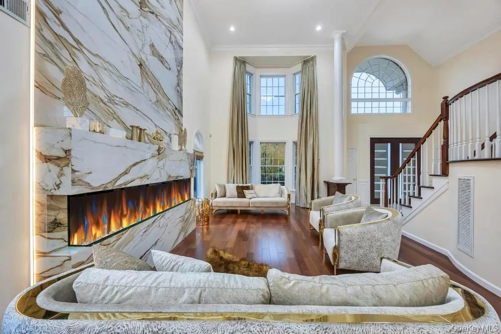 Living area featuring a premium fireplace, dark wood-type flooring, ornamental molding, decorative columns, and stairs Living area featuring a premium fireplace, dark wood-type flooring, ornamental molding, decorative columns, and stairs