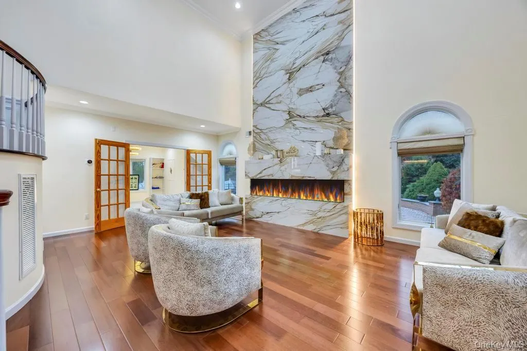 Living area featuring a high end fireplace, a high ceiling, wood-type flooring, french doors, and crown molding Living area featuring a high end fireplace, a high ceiling, wood-type flooring, french doors, and crown molding