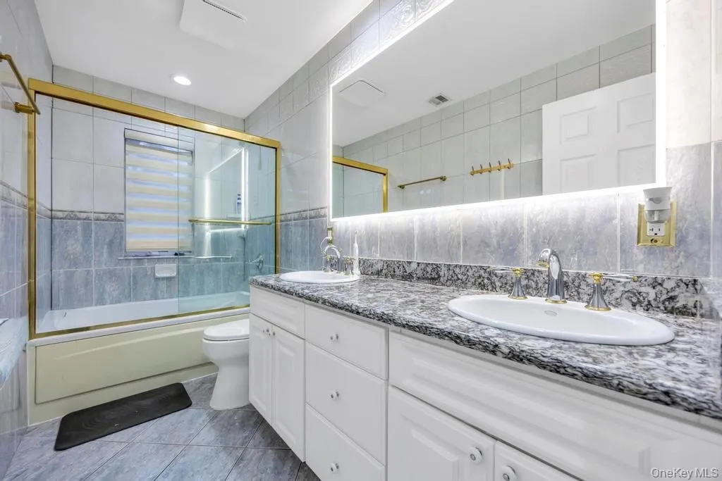 Full bath with combined bath / shower with glass door, double vanity, tile walls, light tile patterned flooring, and recessed lighting Full bath with combined bath / shower with glass door, double vanity, tile walls, light tile patterned flooring, and recessed lighting