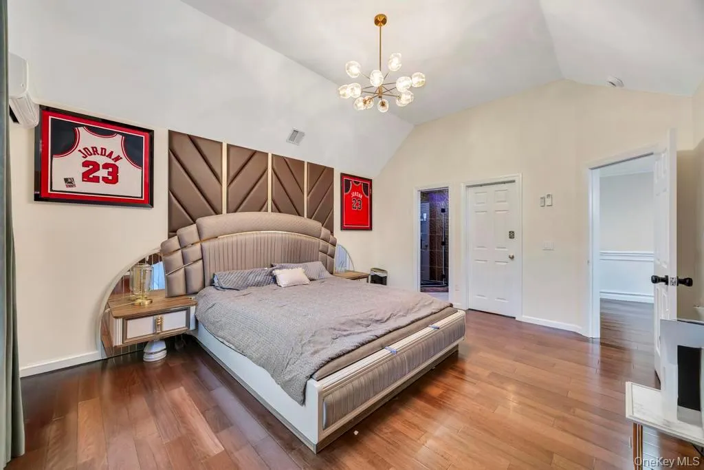 Bedroom with wood finished floors, a chandelier, a wall unit AC, ensuite bath, and high vaulted ceiling Bedroom with wood finished floors, a chandelier, a wall unit AC, ensuite bath, and high vaulted ceiling