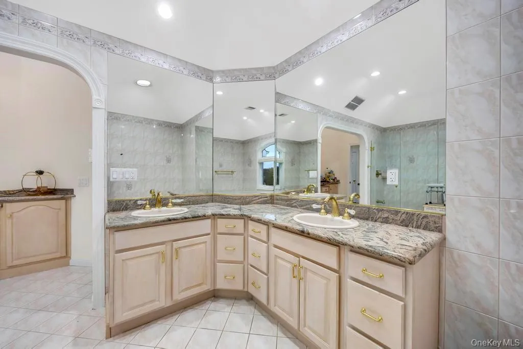 Bathroom with double vanity, light tile patterned flooring, tile walls, and recessed lighting Bathroom with double vanity, light tile patterned flooring, tile walls, and recessed lighting
