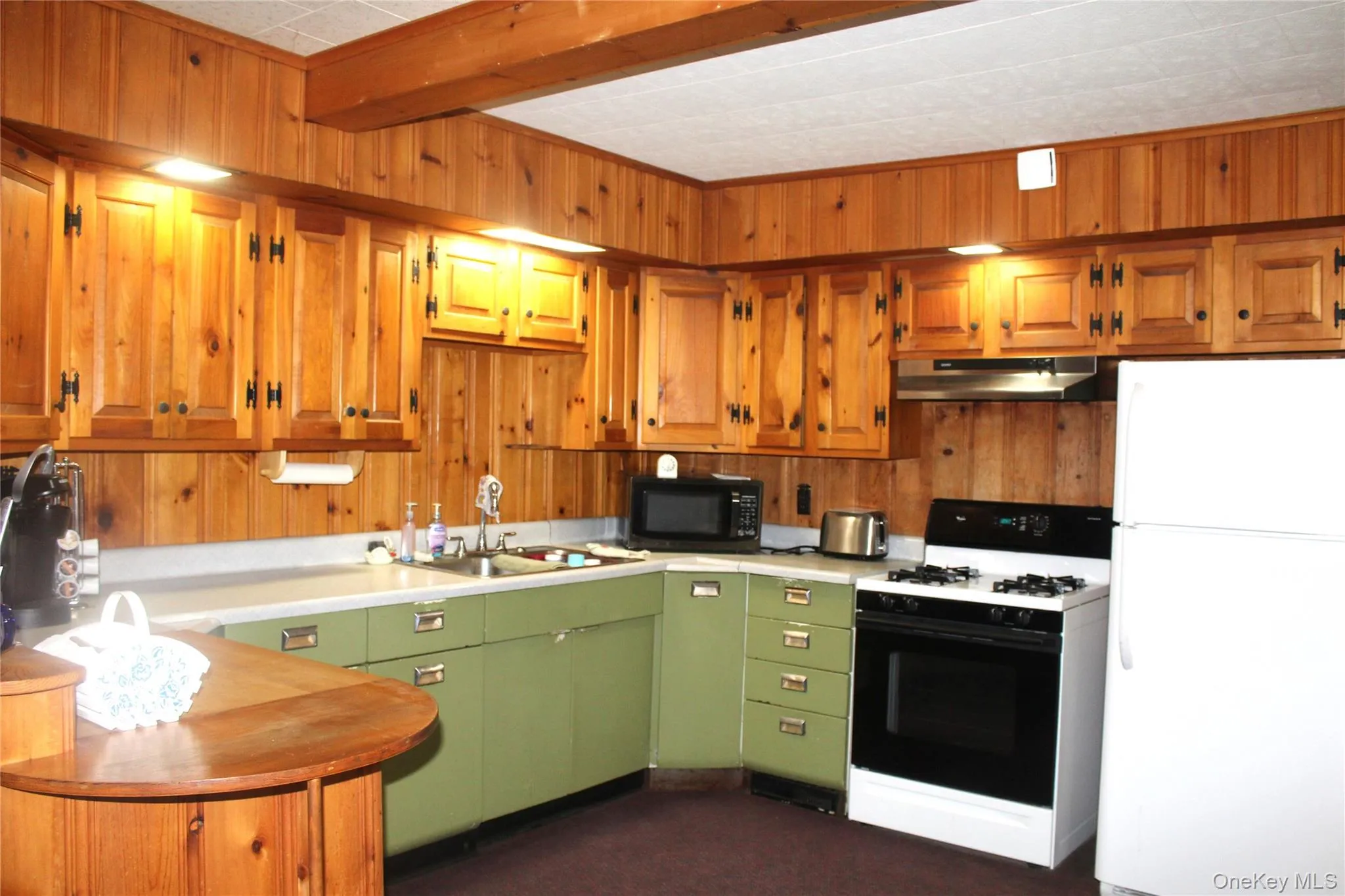 Wood-paneled walls and cabinetry, with a built-in kitchen sink, green lower cabinetry, and a white freestanding range Wood-paneled walls and cabinetry, with a built-in kitchen sink, green lower cabinetry, and a white freestanding range