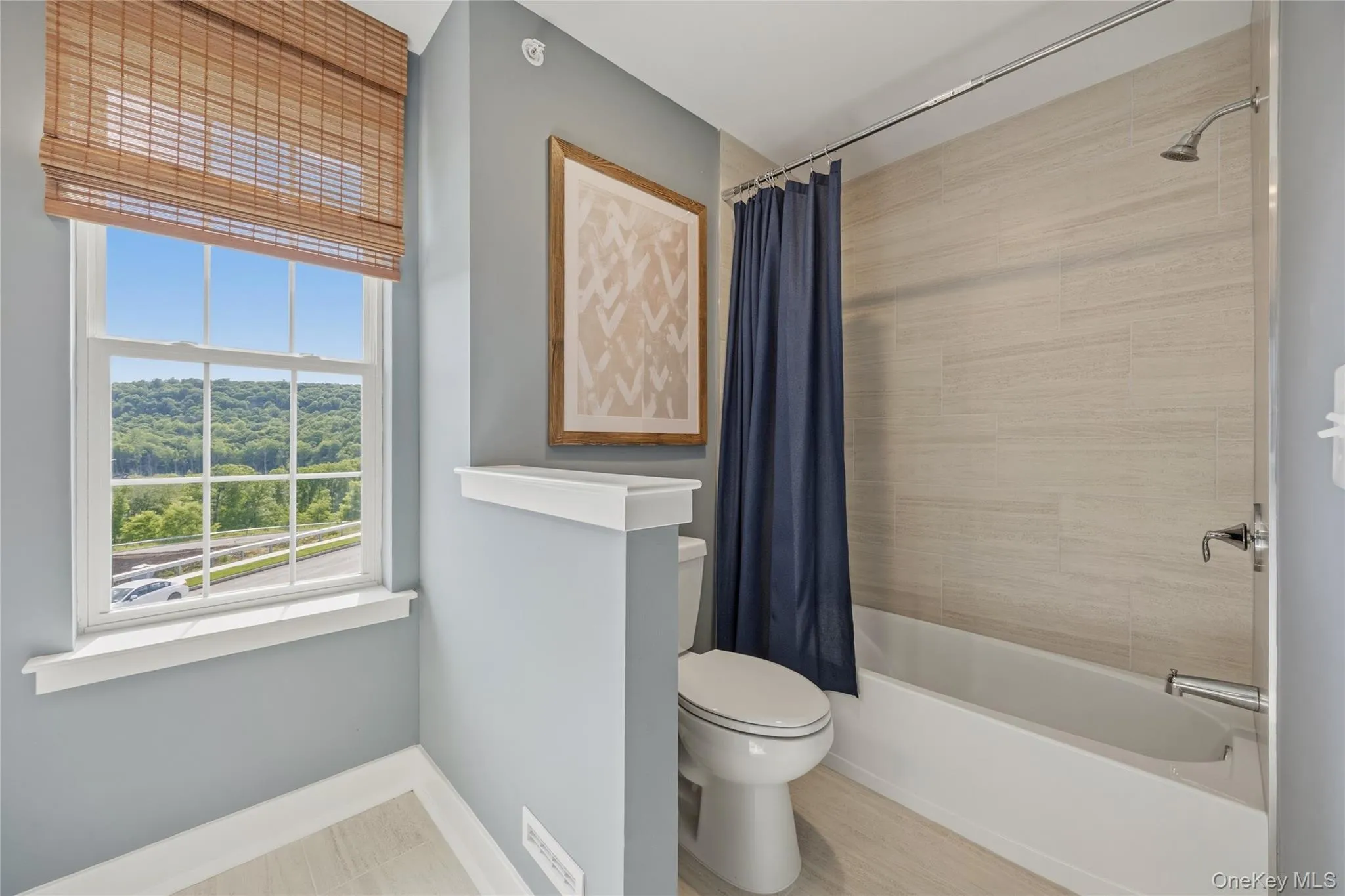Bathroom featuring a window with a mountain backdrop, a full bathtub with a shower, textured wall tile, and light wood-finish flooring Bathroom featuring a window with a mountain backdrop, a full bathtub with a shower, textured wall tile, and light wood-finish flooring