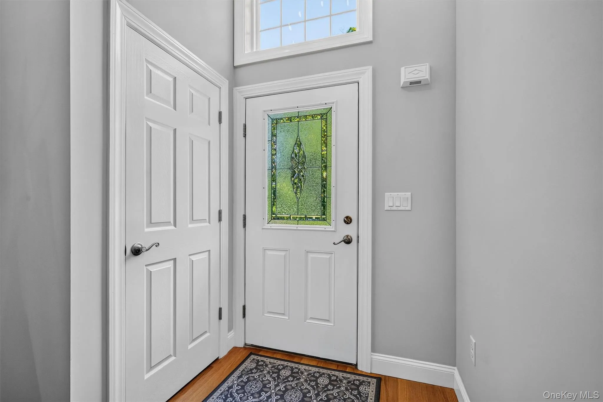 Welcoming entry foyer featuring a striking arched doorway, wide wooden staircase with wooden handrail and metal balusters, warm wood-finish flooring, and a wall-mounted coat rack with hooks for convenient storage Welcoming entry foyer featuring a striking arched doorway, wide wooden staircase with wooden handrail and metal balusters, warm wood-finish flooring, and a wall-mounted coat rack with hooks for convenient storage