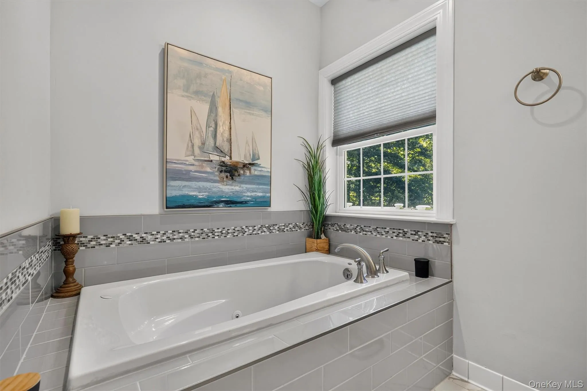 Built-in soaking tub with gray tile surround, mosaic accent tile, and a window with a cellular shade Built-in soaking tub with gray tile surround, mosaic accent tile, and a window with a cellular shade