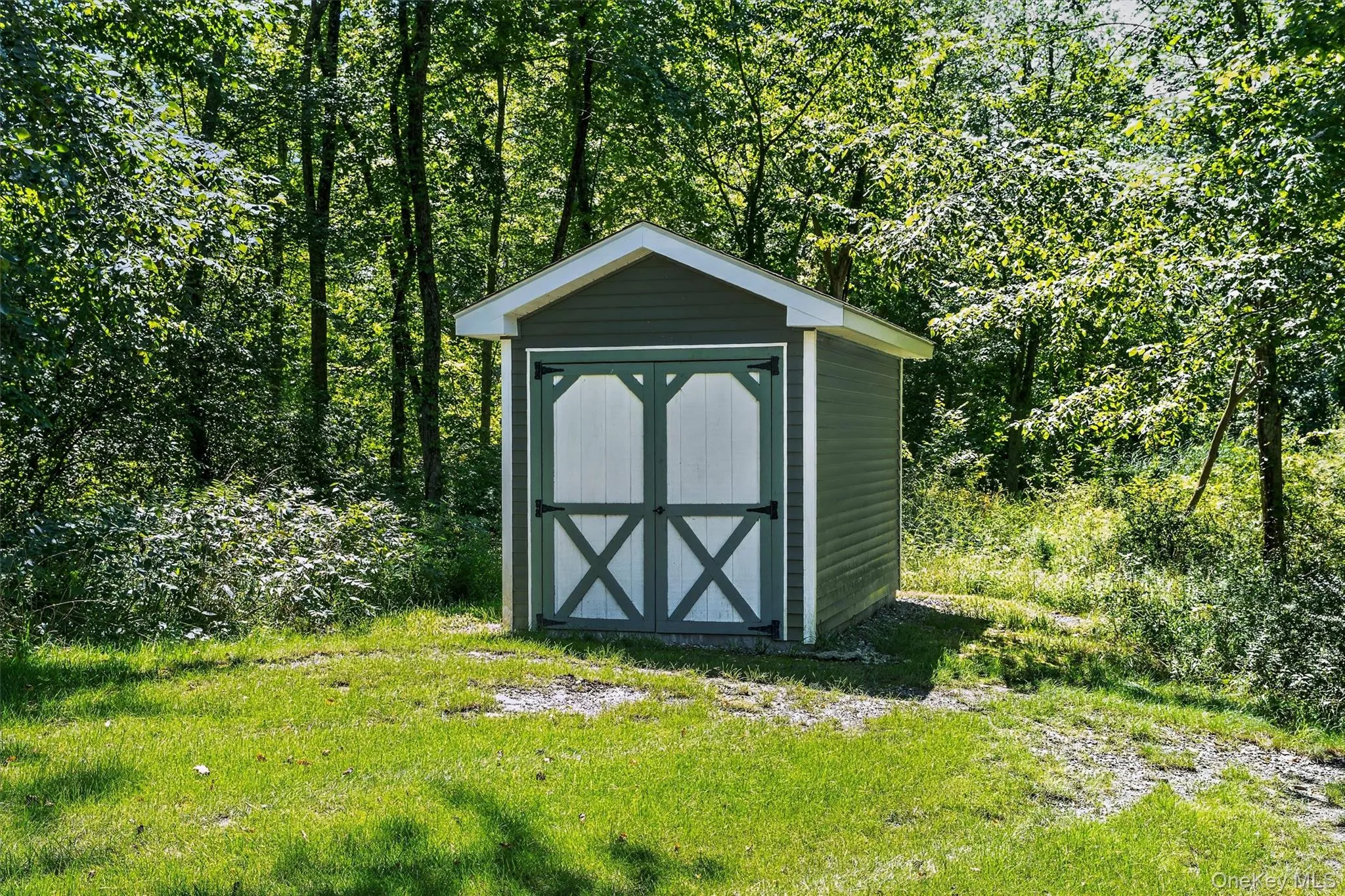 Storage shed with a pitched roof, double doors, and horizontal siding, surrounded by mature trees and a grassy area Storage shed with a pitched roof, double doors, and horizontal siding, surrounded by mature trees and a grassy area