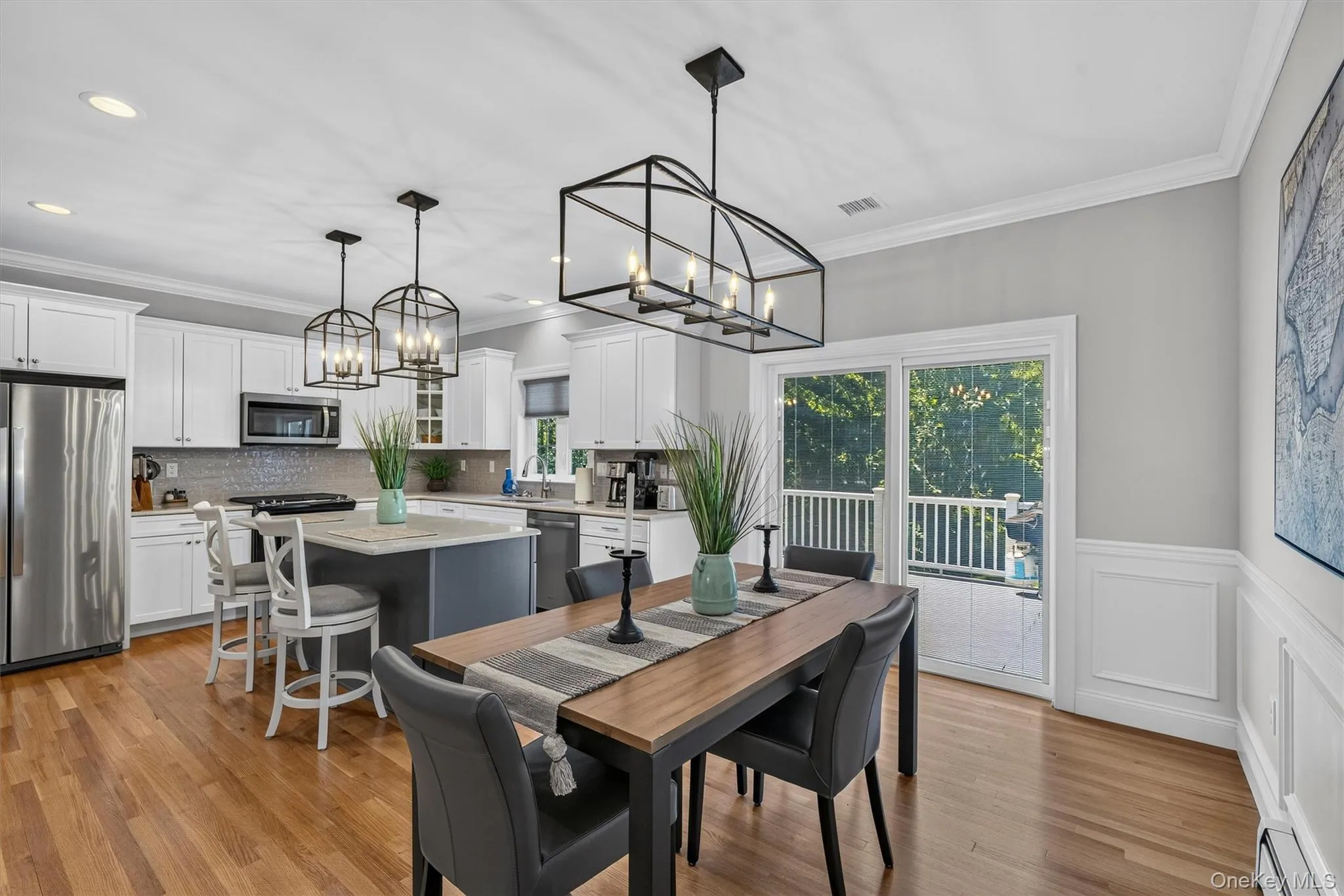 Hardwood flooring, white shaker cabinetry, stainless steel appliances, central island with seating, and a sliding glass door Hardwood flooring, white shaker cabinetry, stainless steel appliances, central island with seating, and a sliding glass door