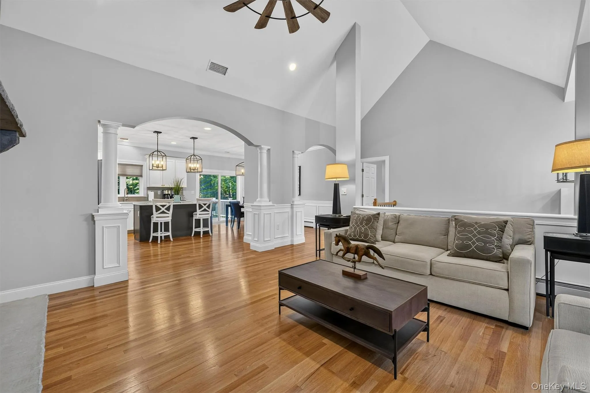 Open-concept living area showcasing soaring ceilings with architectural beams, hardwood flooring throughout, and abundant natural light from recessed fixtures Open-concept living area showcasing soaring ceilings with architectural beams, hardwood flooring throughout, and abundant natural light from recessed fixtures