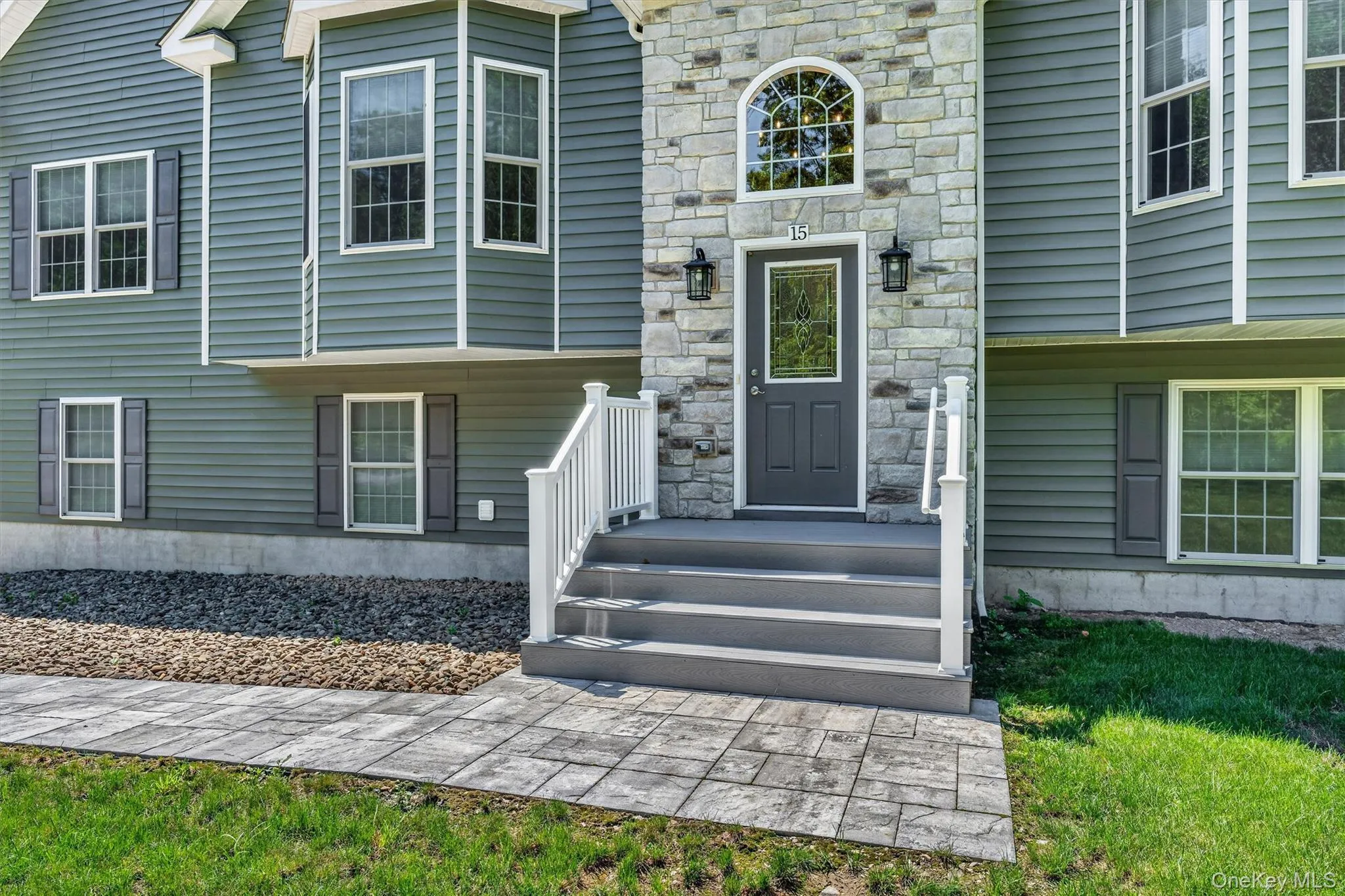 Welcoming front entry featuring a stone chimney accent wall, multi-pane transom window, and dark composite entry door Welcoming front entry featuring a stone chimney accent wall, multi-pane transom window, and dark composite entry door