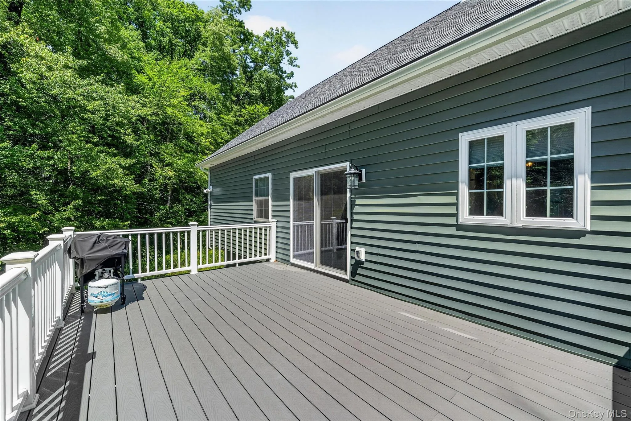 Spacious outdoor deck with composite decking, white railings, dark green siding, and double-pane windows Spacious outdoor deck with composite decking, white railings, dark green siding, and double-pane windows