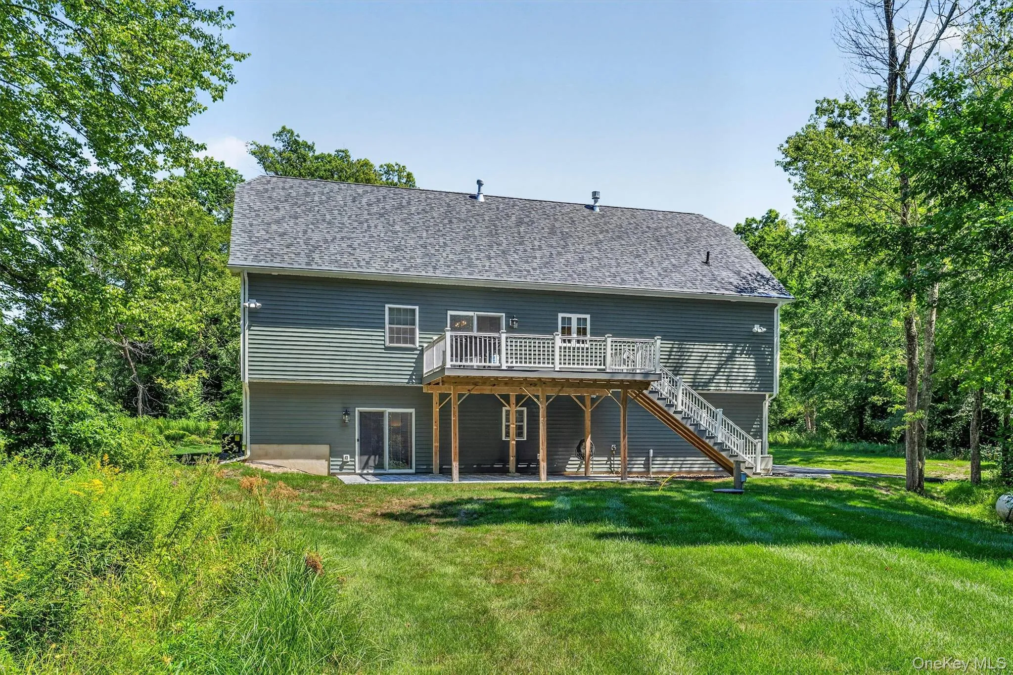 Rear exterior featuring a grey shingle roof, green horizontal siding, and a wood deck with white railings Rear exterior featuring a grey shingle roof, green horizontal siding, and a wood deck with white railings