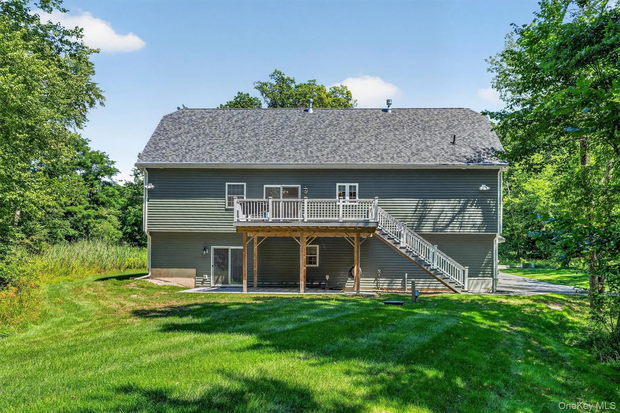 Rear exterior featuring two levels of siding, a second-story deck with white railings, exterior stairs, a ground-level patio, and a shingle roof Rear exterior featuring two levels of siding, a second-story deck with white railings, exterior stairs, a ground-level patio, and a shingle roof