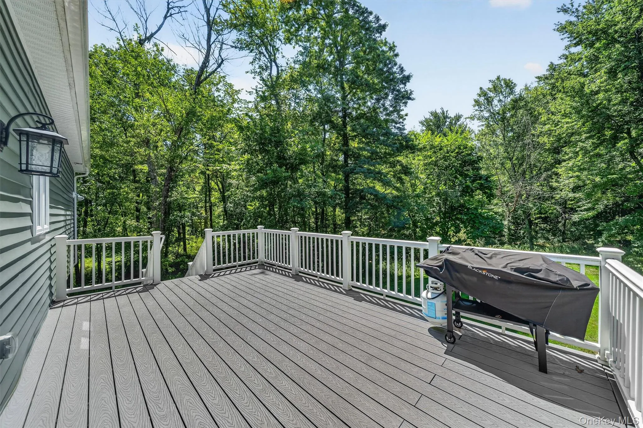 Spacious outdoor deck featuring composite decking, white railing, and exterior wall lighting Spacious outdoor deck featuring composite decking, white railing, and exterior wall lighting