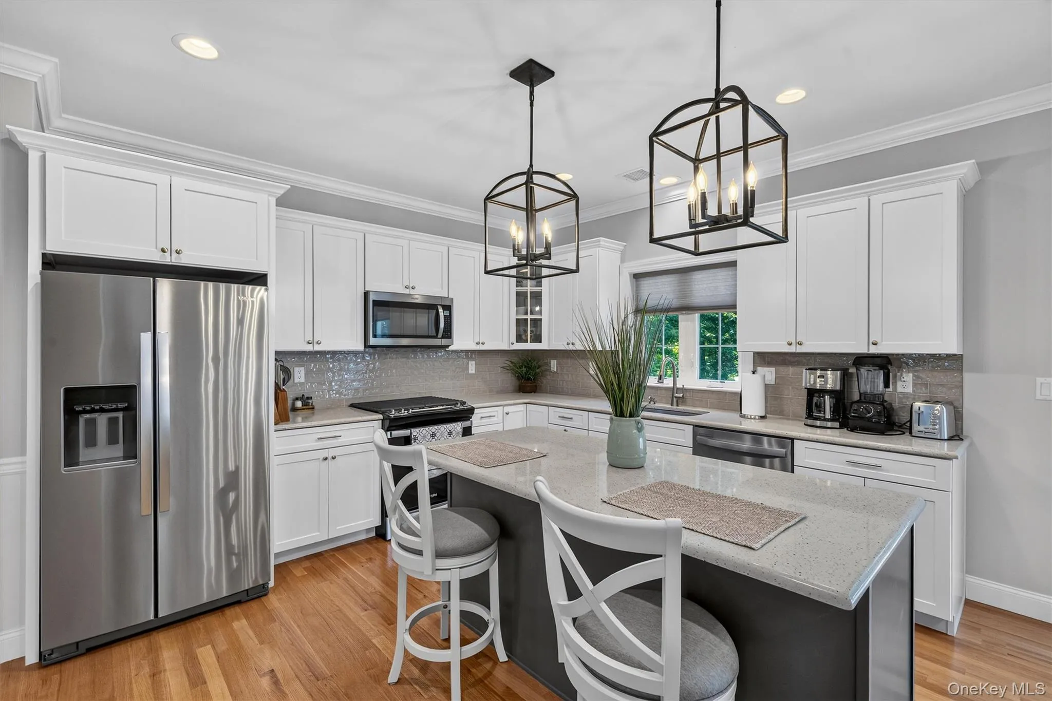 Chef's kitchen featuring white shaker cabinetry, stainless steel appliances including a French-door refrigerator and gas cooktop, quartz countertops, gray subway tile backsplash, and a two-tier island with seating Chef's kitchen featuring white shaker cabinetry, stainless steel appliances including a French-door refrigerator and gas cooktop, quartz countertops, gray subway tile backsplash, and a two-tier island with seating