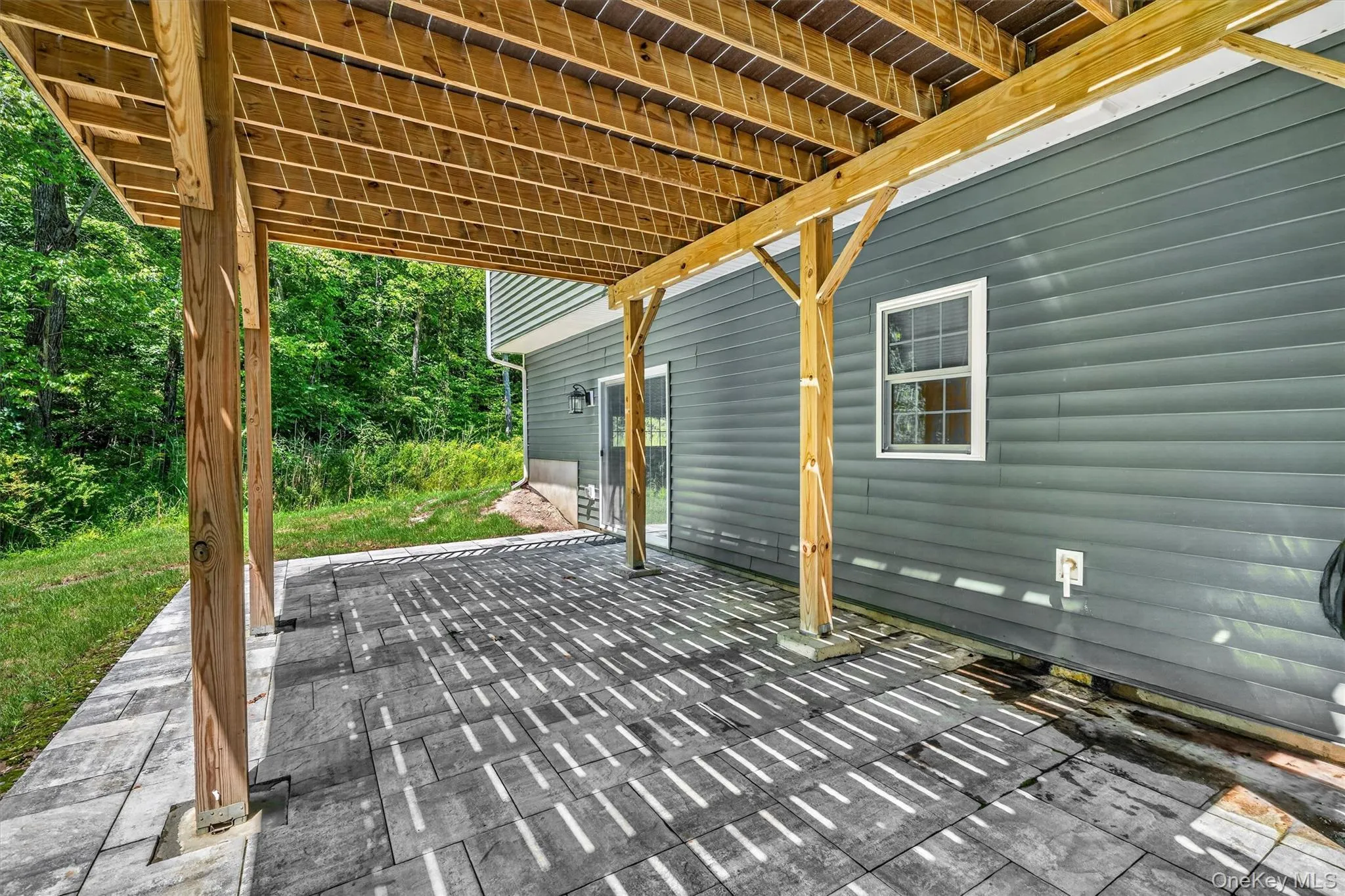 Covered patio with a paver surface, supported by exposed wood beams and posts Covered patio with a paver surface, supported by exposed wood beams and posts