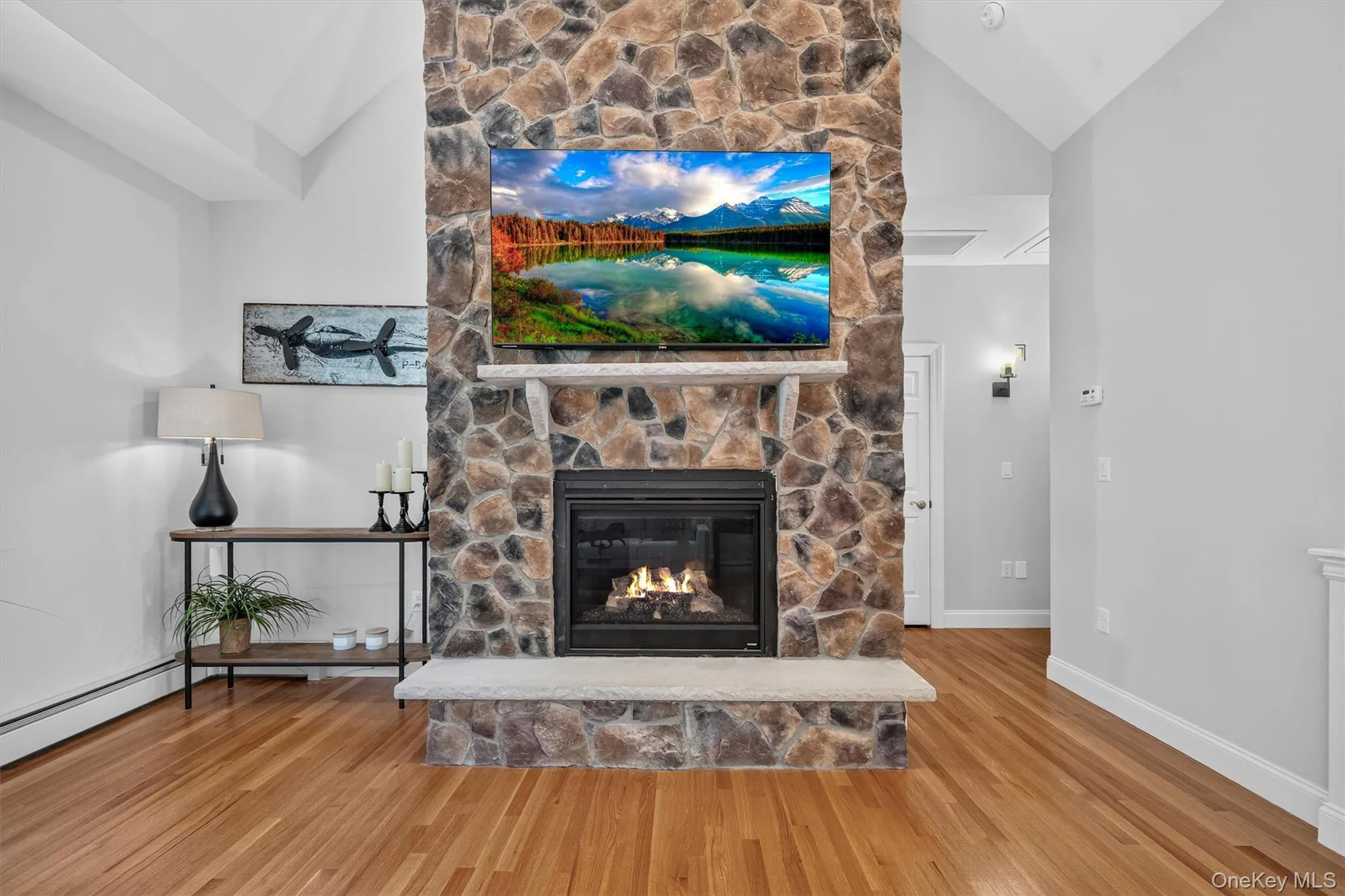 Stacked stone fireplace with a raised hearth, wood-finish flooring, vaulted ceiling, and recessed lighting Stacked stone fireplace with a raised hearth, wood-finish flooring, vaulted ceiling, and recessed lighting