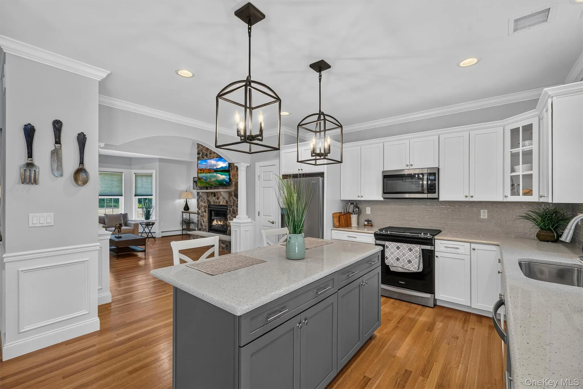 Kitchen featuring white upper cabinetry, a gray kitchen island with stone countertops, and wood-finish flooring Kitchen featuring white upper cabinetry, a gray kitchen island with stone countertops, and wood-finish flooring