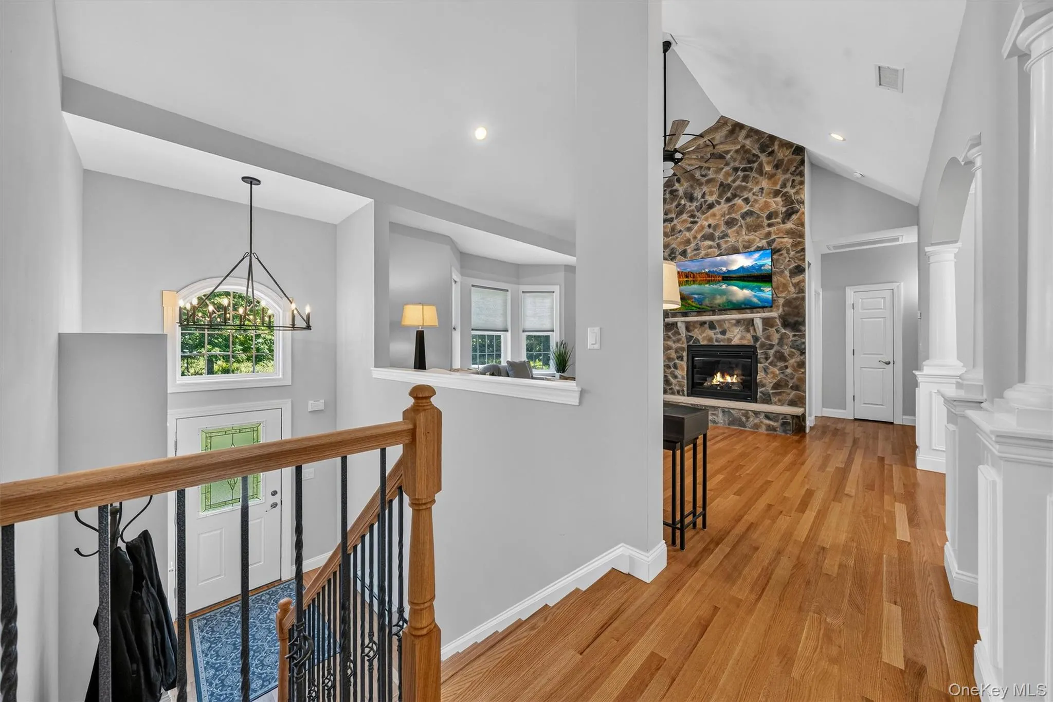 Hardwood flooring, stone-clad fireplace with mantel, vaulted ceiling, wrought iron stair railing with wood-finish top rail, arched entryway with decorative columns Hardwood flooring, stone-clad fireplace with mantel, vaulted ceiling, wrought iron stair railing with wood-finish top rail, arched entryway with decorative columns