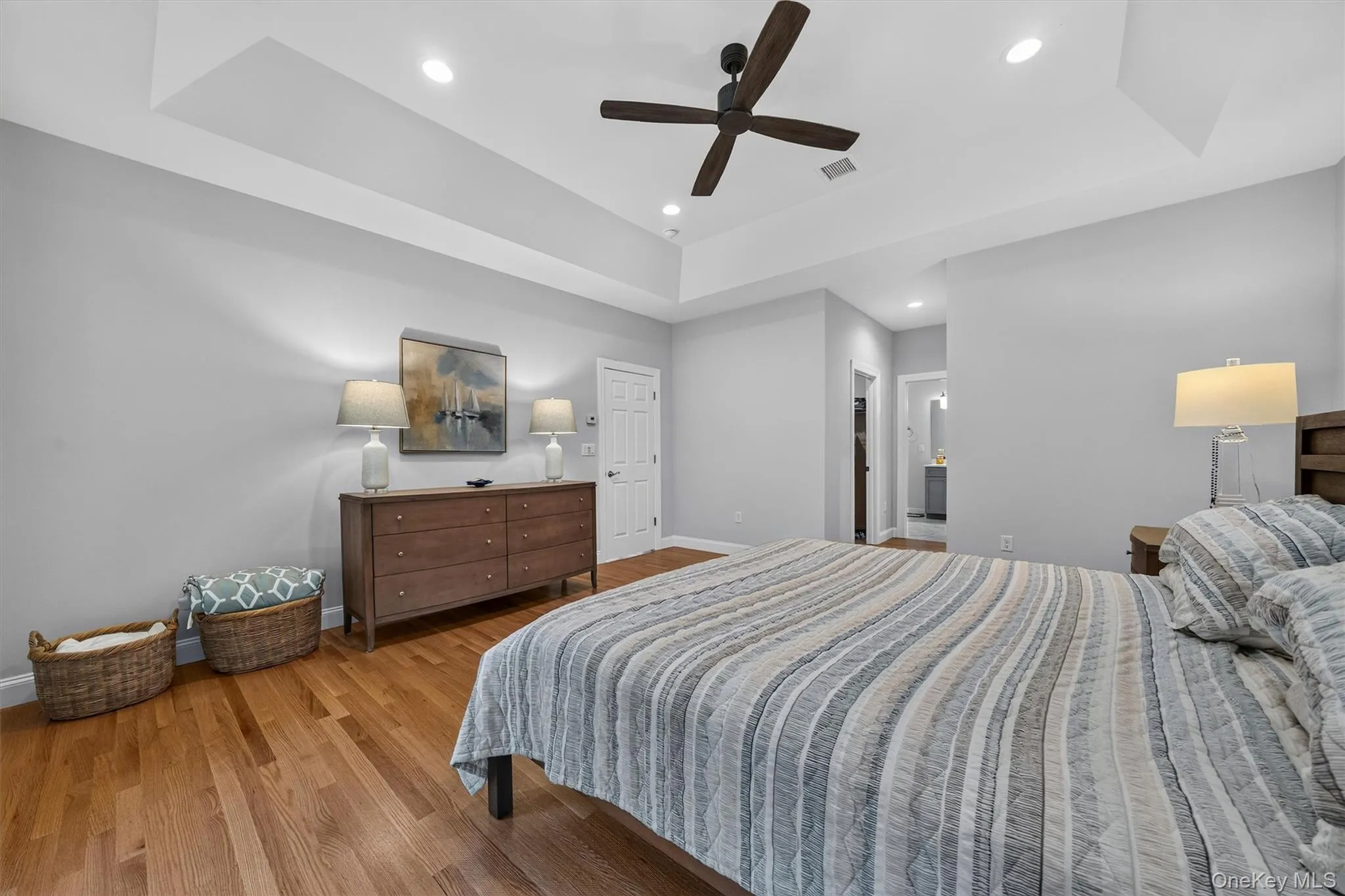 Tray ceiling with recessed lighting, wood-finish flooring, and a ceiling fan Tray ceiling with recessed lighting, wood-finish flooring, and a ceiling fan