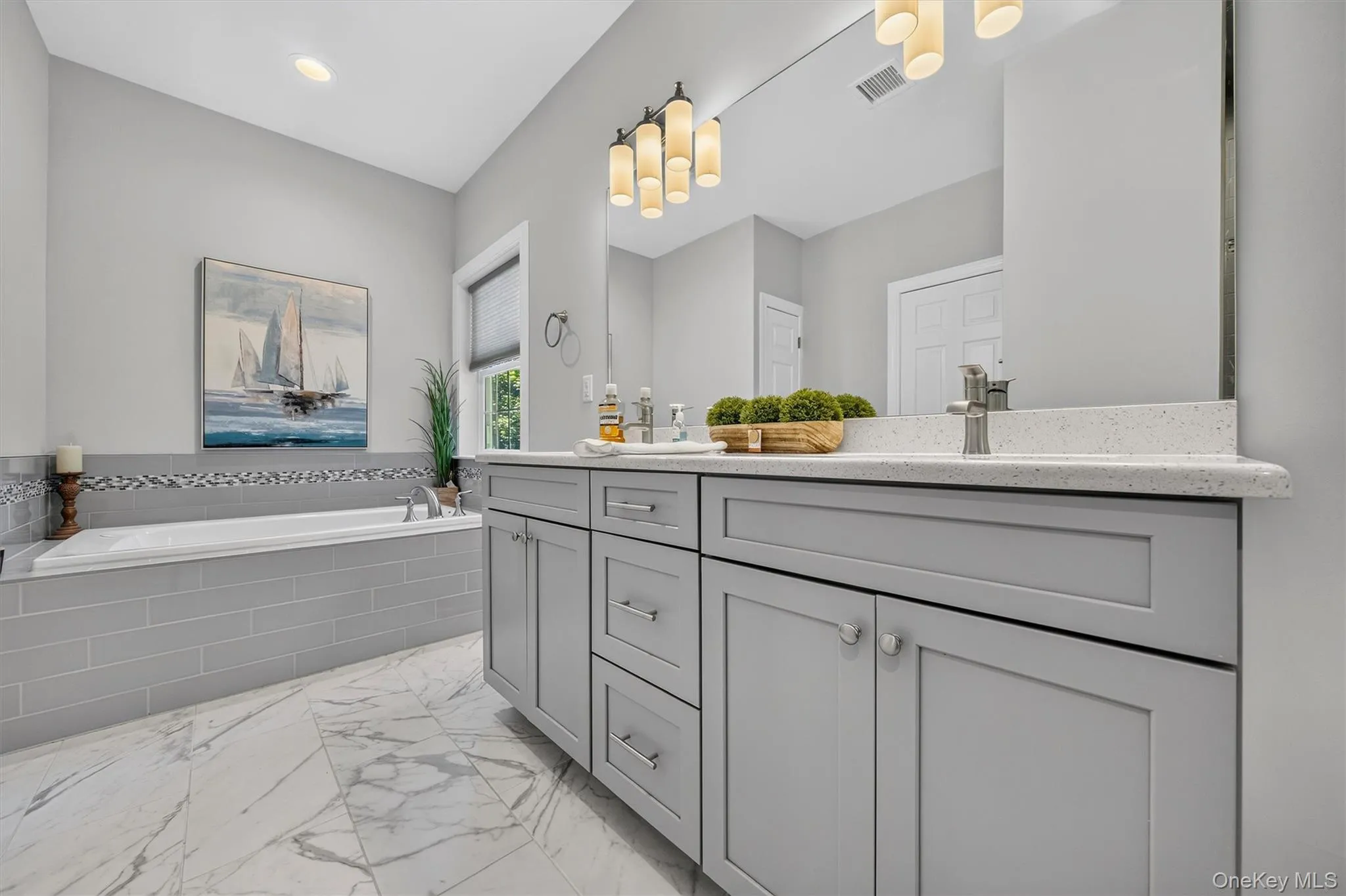Double vanity with light gray shaker-style cabinetry, white speckled countertop, and brushed nickel hardware Double vanity with light gray shaker-style cabinetry, white speckled countertop, and brushed nickel hardware
