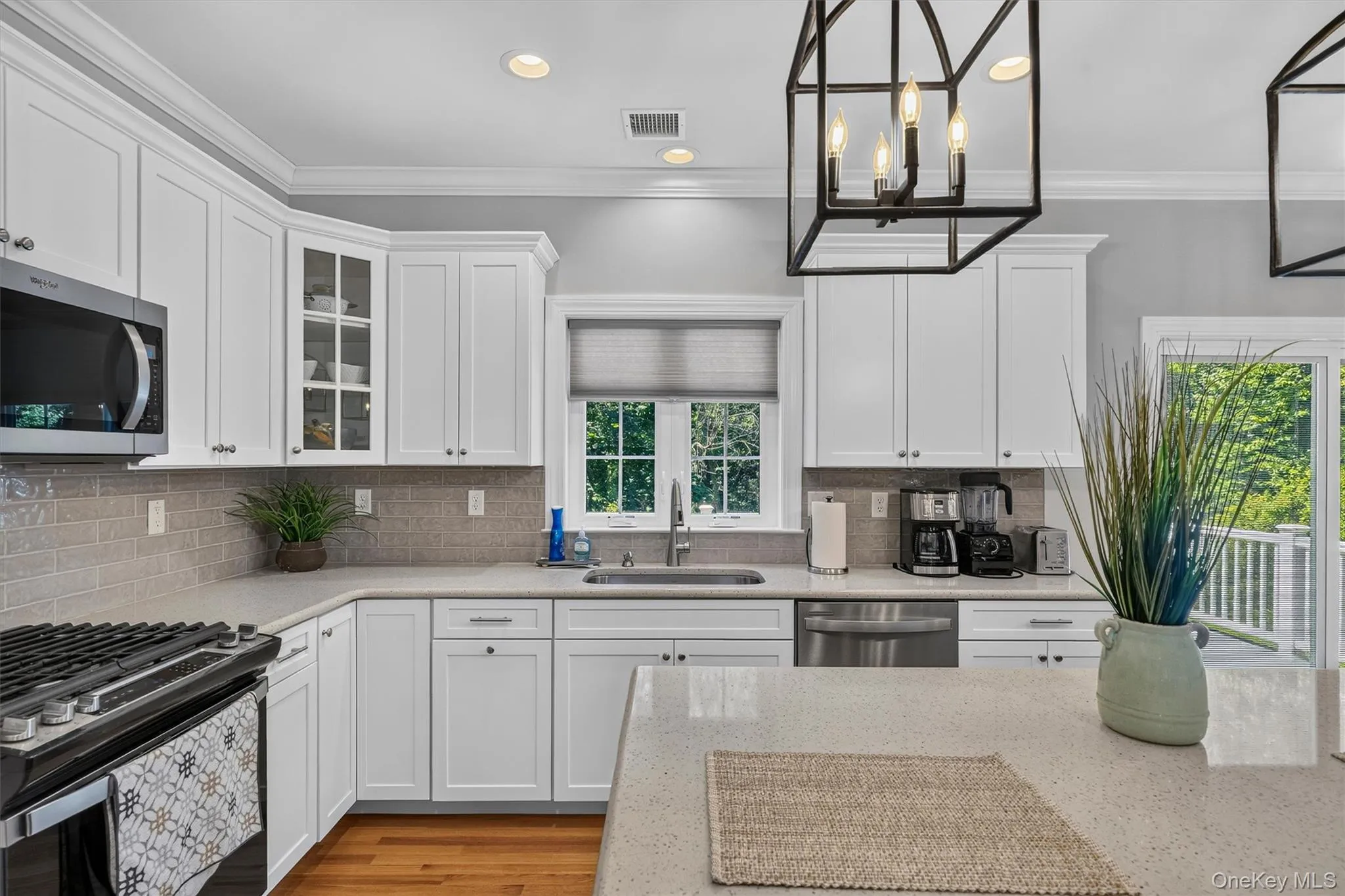 Bright, chef's kitchen featuring crisp white cabinetry with glass-front upper cabinets, stainless steel appliances including a professional-grade gas cooktop, quartz countertops, subway tile backsplash, and abundant natural light from multiple windows Bright, chef's kitchen featuring crisp white cabinetry with glass-front upper cabinets, stainless steel appliances including a professional-grade gas cooktop, quartz countertops, subway tile backsplash, and abundant natural light from multiple windows
