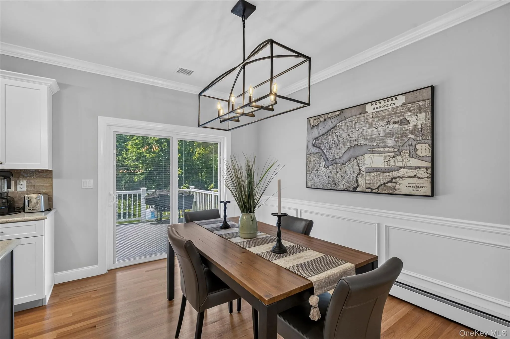 Elegant dining room featuring hardwood flooring, a geometric metal pendant light fixture, and wainscoting detail Elegant dining room featuring hardwood flooring, a geometric metal pendant light fixture, and wainscoting detail