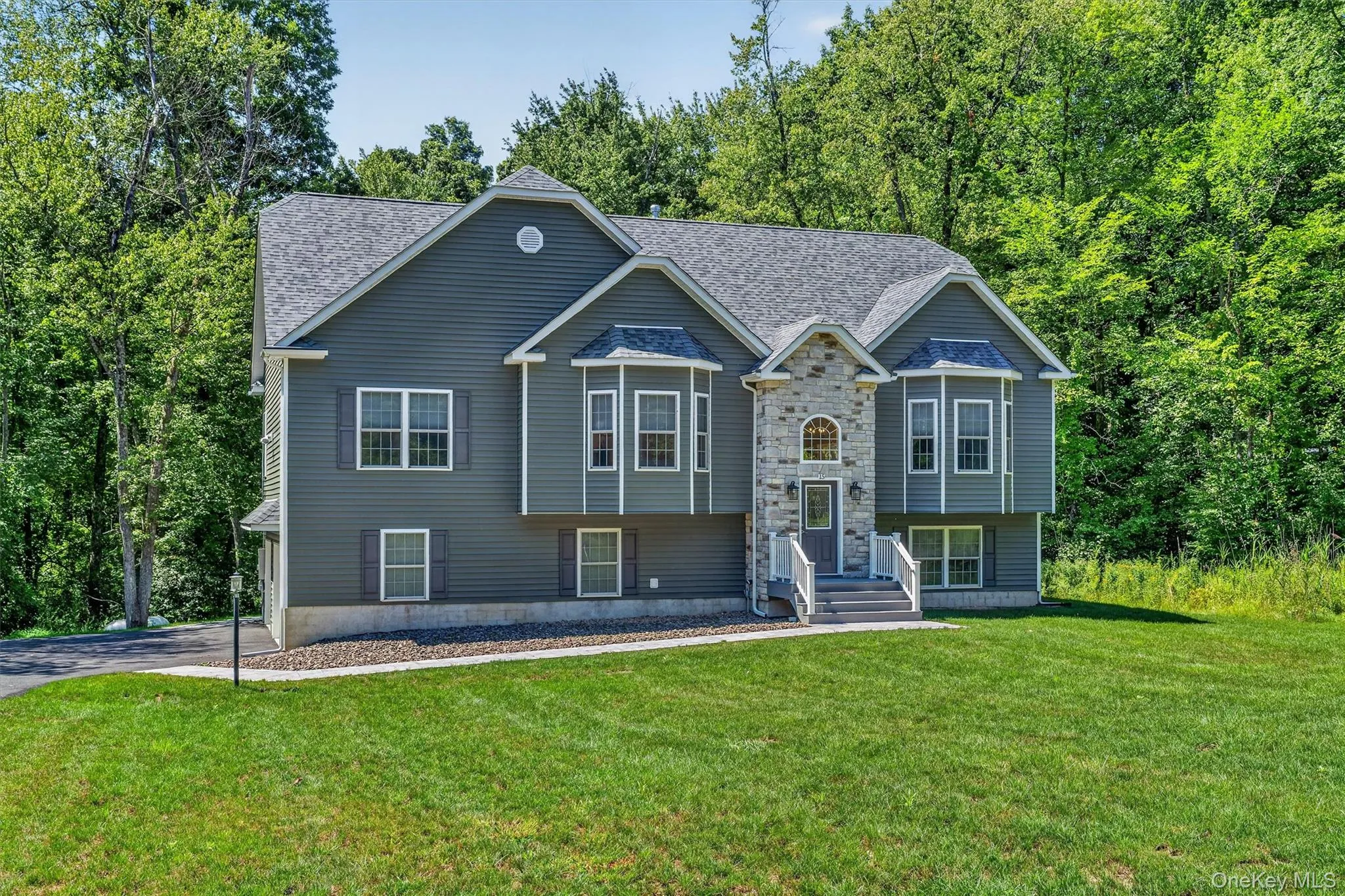 Exterior featuring gray siding, stone veneer accents, multiple window bays, an arched entry door, and a gray shingle roof Exterior featuring gray siding, stone veneer accents, multiple window bays, an arched entry door, and a gray shingle roof