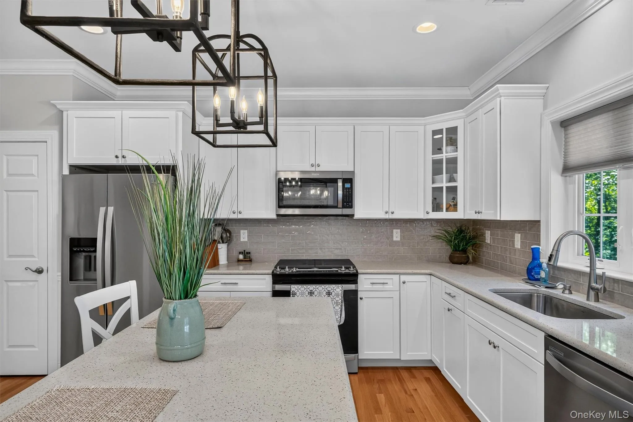 White shaker cabinetry, stainless steel appliances, light-toned countertops, tile backsplash, and wood-finish flooring White shaker cabinetry, stainless steel appliances, light-toned countertops, tile backsplash, and wood-finish flooring