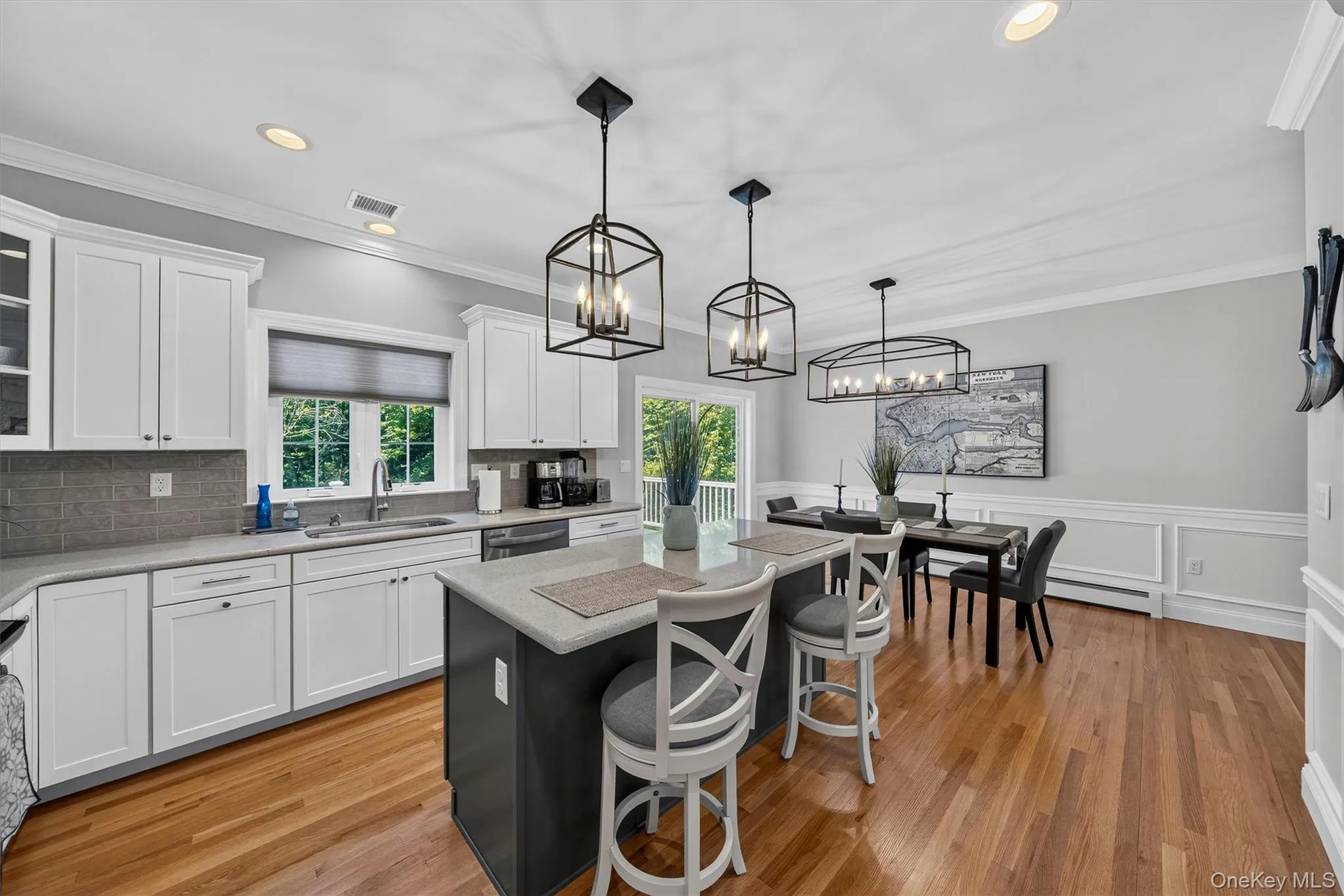 Open-concept kitchen and dining area featuring white cabinetry, stainless steel appliances, wood-finish flooring, a center island with seating for multiple guests, and pendant lighting suspended from the ceiling Open-concept kitchen and dining area featuring white cabinetry, stainless steel appliances, wood-finish flooring, a center island with seating for multiple guests, and pendant lighting suspended from the ceiling