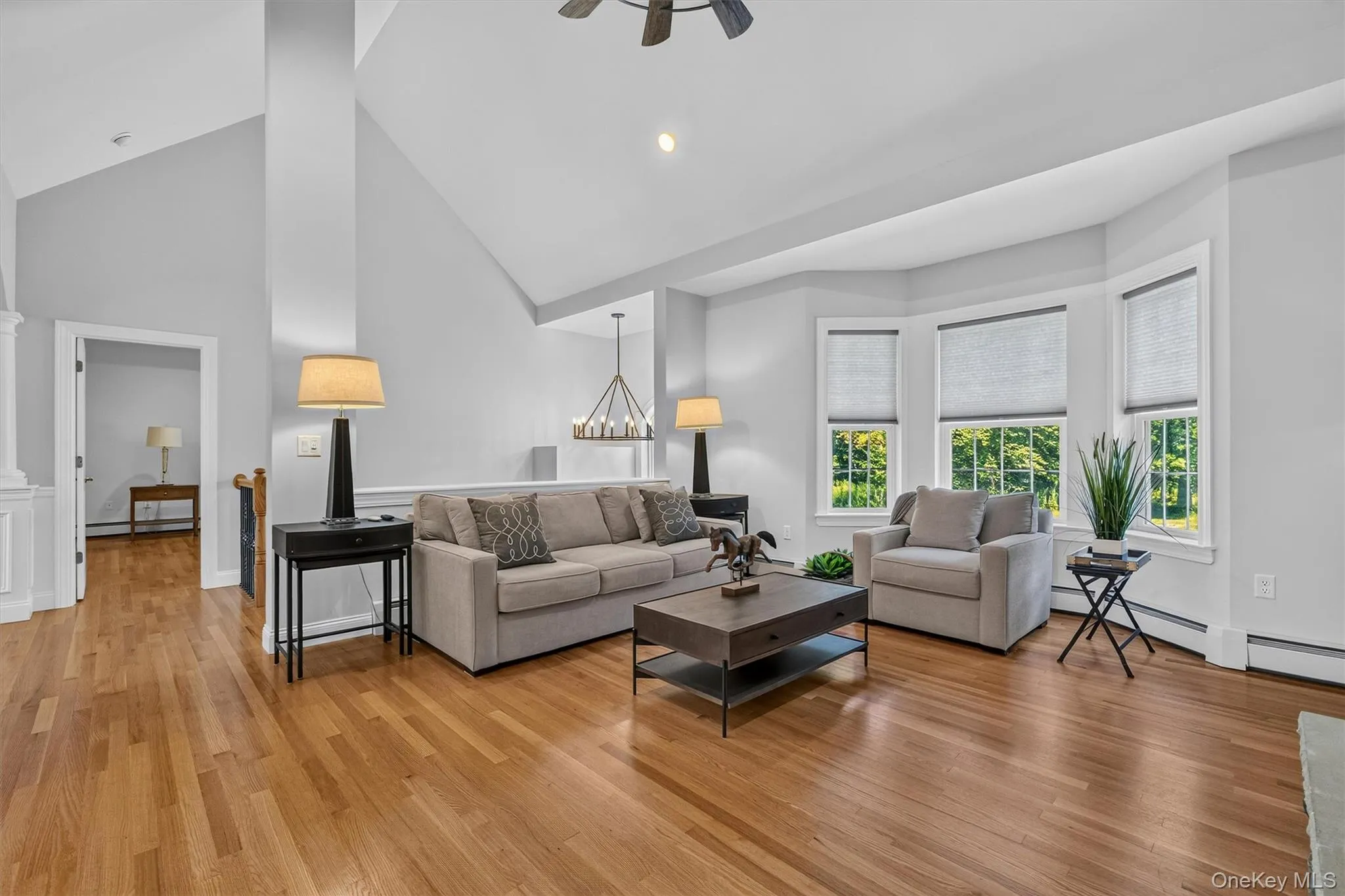 Bright, open living area showcasing hardwood flooring throughout, vaulted ceilings with recessed lighting, and expansive windows with integrated blinds flooding the space with natural light Bright, open living area showcasing hardwood flooring throughout, vaulted ceilings with recessed lighting, and expansive windows with integrated blinds flooding the space with natural light