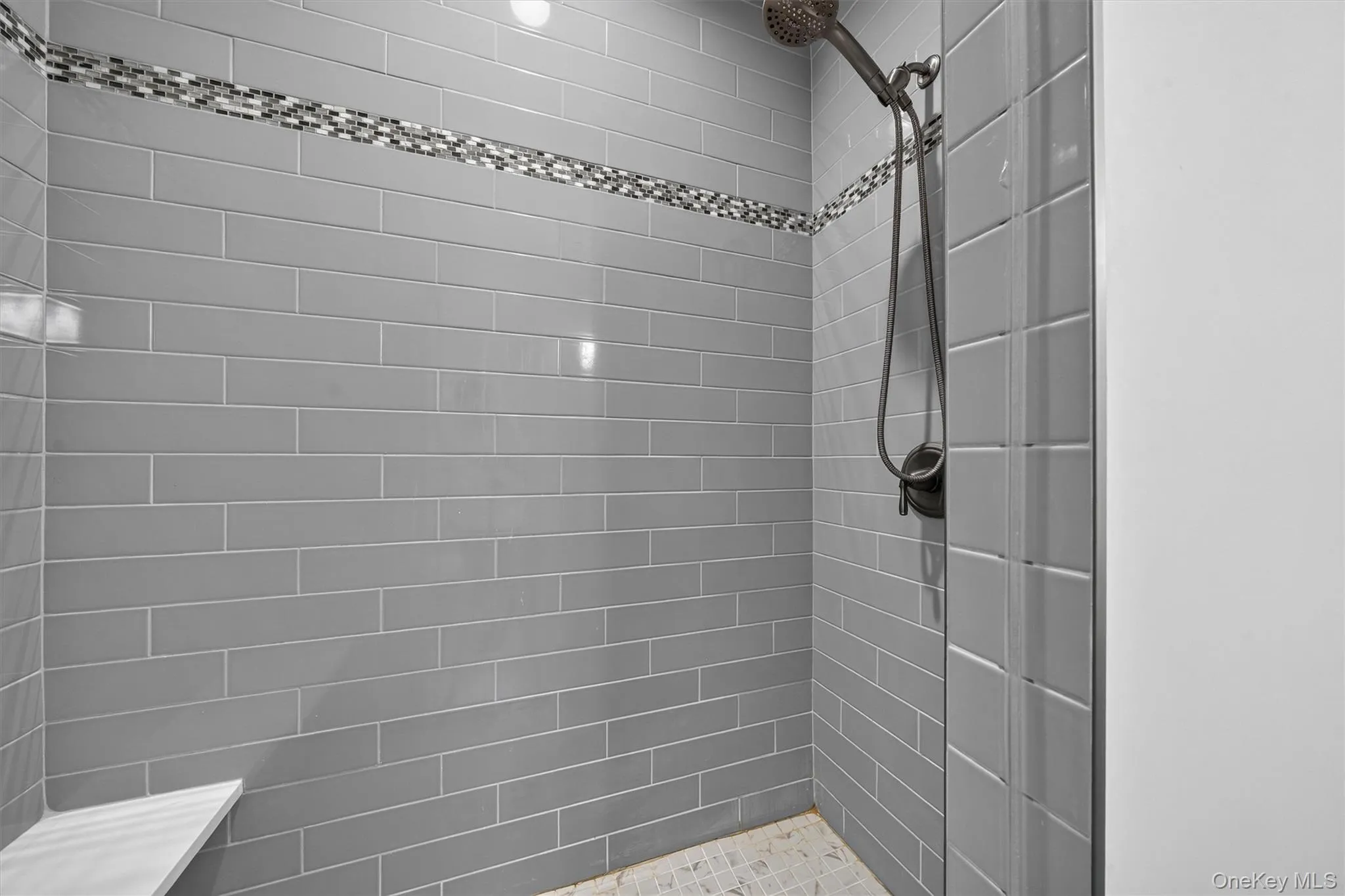 Shower with gray subway tile surround, mosaic accent band, built-in corner bench, and dark-finish shower fixtures Shower with gray subway tile surround, mosaic accent band, built-in corner bench, and dark-finish shower fixtures