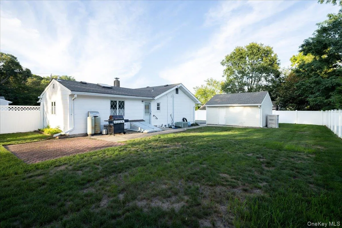 Expansive rear yard featuring a paved patio, white privacy fencing, and a detached auxiliary structure Expansive rear yard featuring a paved patio, white privacy fencing, and a detached auxiliary structure