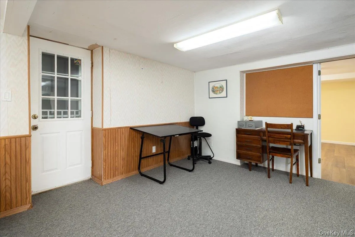 Carpeted room with beadboard wainscoting and a white door with windowpanes Carpeted room with beadboard wainscoting and a white door with windowpanes